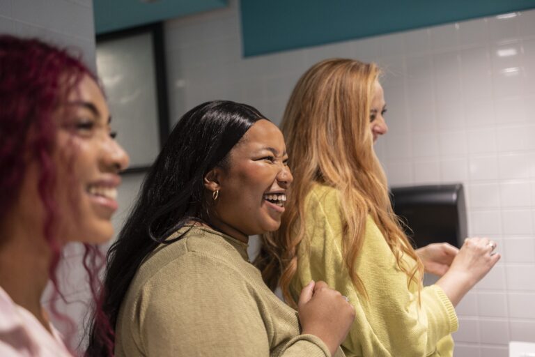 Three diverse young women smiling and laughing together, fostering connection and positivity in the workplace.