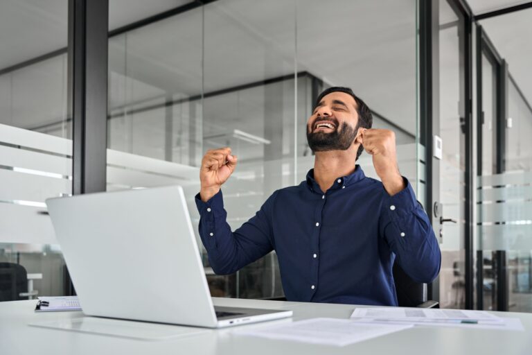 Smiling employee celebrating success while working on a laptop in a modern office, representing motivation and engagement from virtual employee incentives.