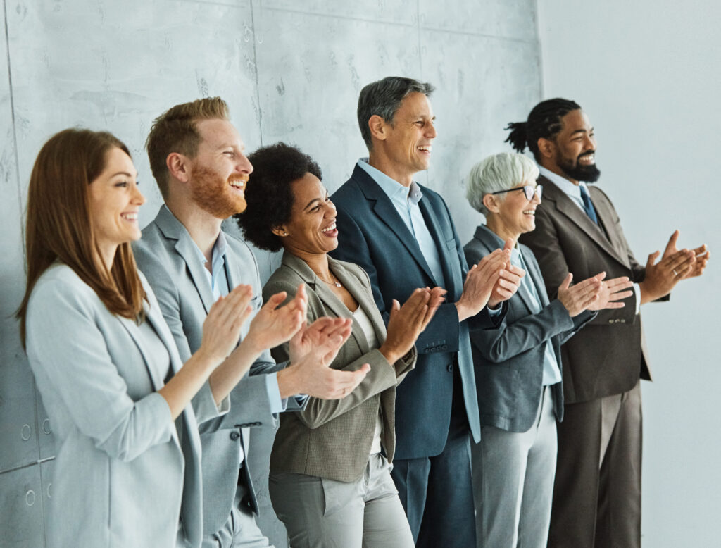 A diverse group of professionals standing in a row clapping and smiling, symbolizing employee recognition, appreciation, and positive workplace culture.