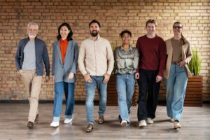 A diverse group of six smiling professionals walks confidently together inside a modern office space, symbolizing teamwork, culture, and strong people operations.