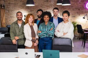 Diverse group of smiling startup team members standing confidently together in a modern open office, representing strong company culture and collaboration.