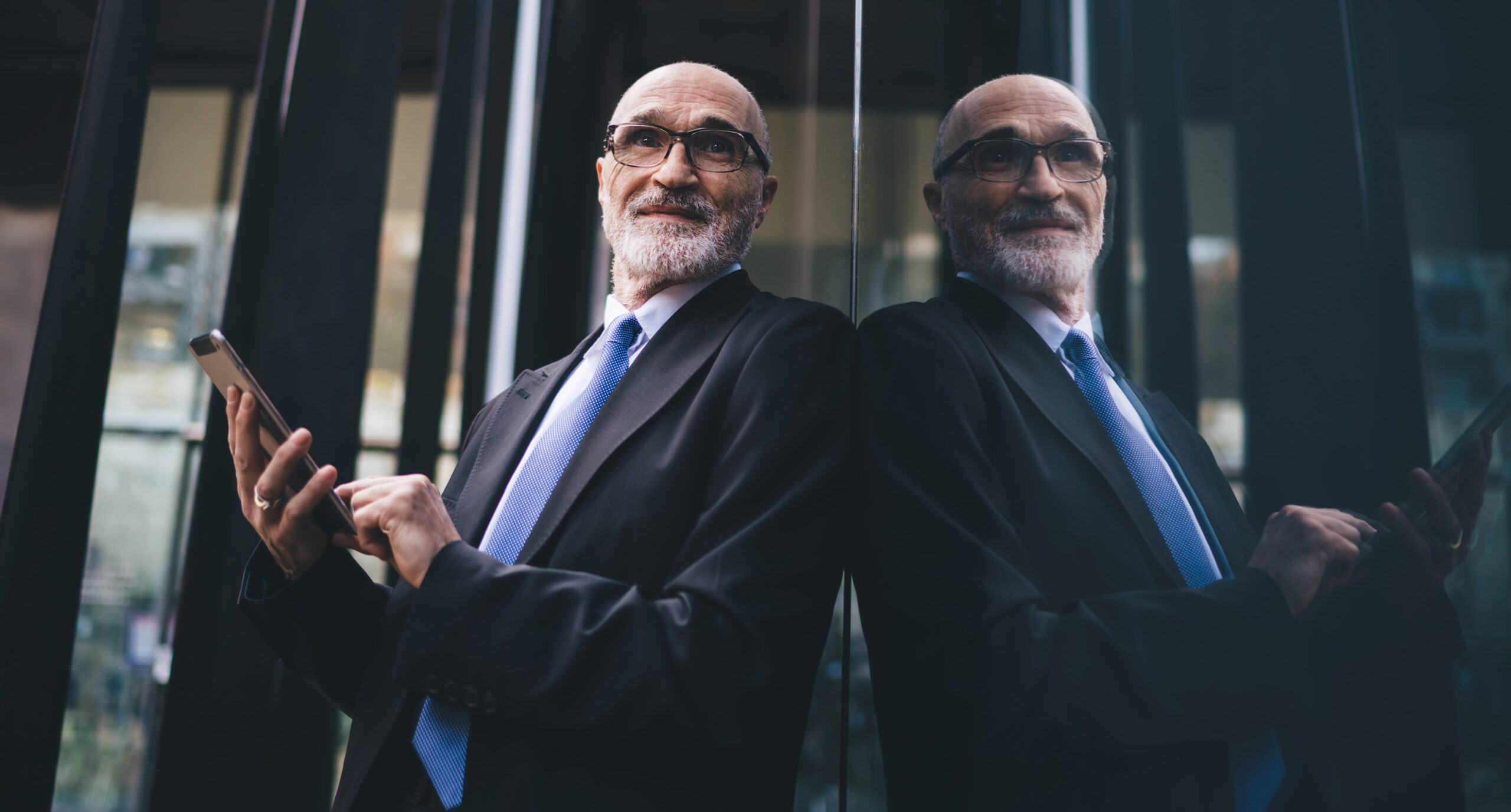 Thoughtful senior business leader holding a smartphone, reflecting on leadership growth and the transition from hands-on founder to strategic leader, with a modern office backdrop.