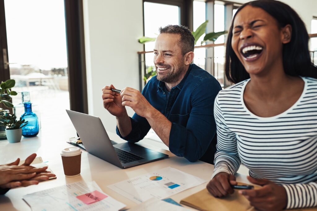 A group of coworkers smiling and laughing together during a meeting, reflecting strong team happiness, connection, and a positive startup culture.
