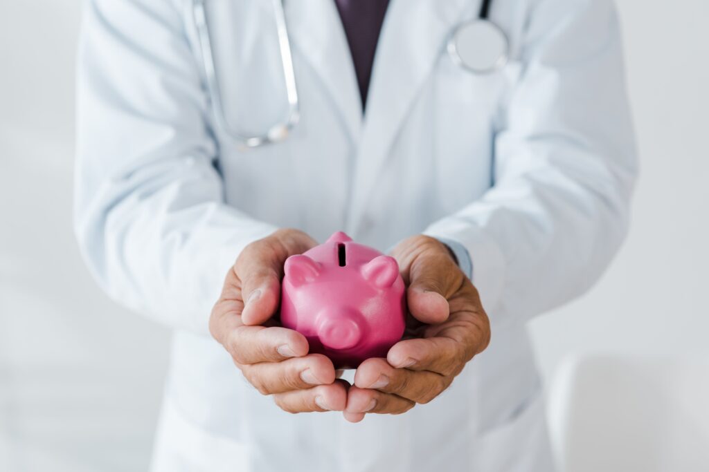 A doctor in a white coat holds a pink piggy bank, symbolizing healthcare cost savings and the ROI of prevention for TPAs and employer groups.