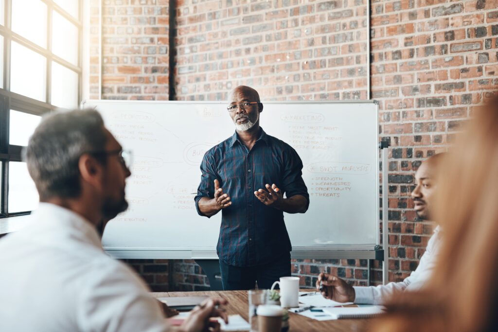 A founder-style leader stands in front of a whiteboard presenting to a team, modeling strong communication and a culture of openness and alignment.