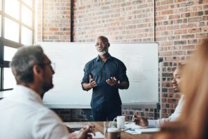 A founder-style leader stands in front of a whiteboard presenting to a team, modeling strong communication and a culture of openness and alignment.