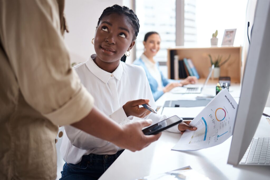 A young professional reviewing data charts at her desk while discussing information with a colleague, representing collaborative decision-making around non-GLP-1 wellness strategies for TPAs.