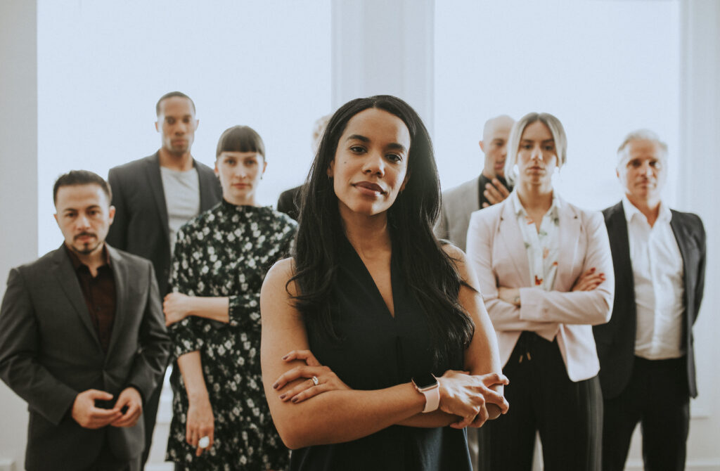 Confident VP of People standing at the front of a diverse leadership team in a modern office, representing people leadership, workforce strategy, and human-centered risk management.