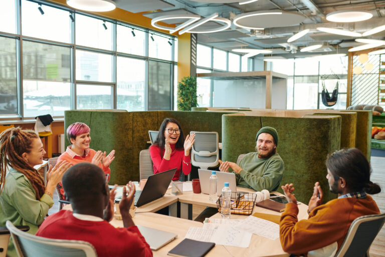 A diverse group of employees clapping and celebrating together in a modern office, representing a successful culture initiative launch, team engagement, and shared momentum.