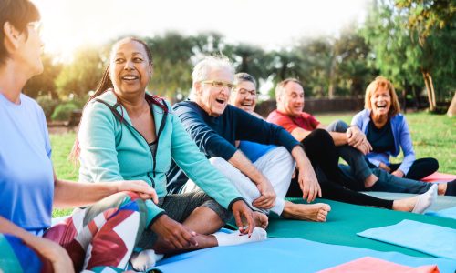 A diverse group of adults sitting on yoga mats outdoors, smiling and talking after a group wellness session, representing personalized wellbeing and community-focused health support.