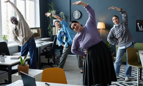 Employees stretching together during a workplace wellness break, illustrating how daily engagement activities support long-term workforce health outcomes and prevention.